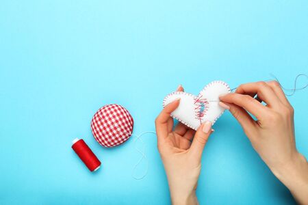 Female hands sewing broken fabric heart by needle and thread on blue backgroundの写真素材