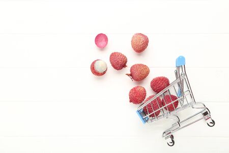 Tasty lychee with shopping cart on white wooden table