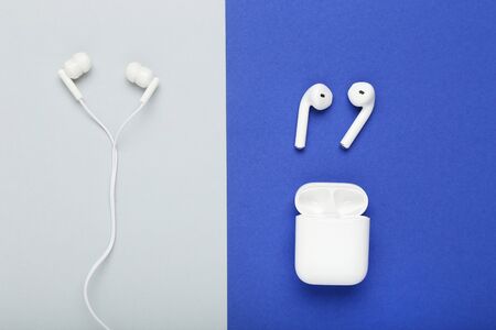 White earphones with wireless earbuds on blue and grey background