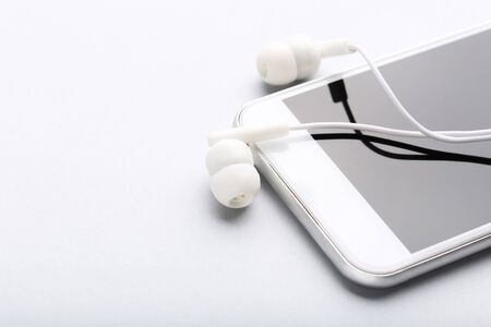 Earphones with mobile phone on grey background