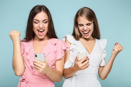 Young happy girlfriends with mobile phones on blue backgroundの写真素材
