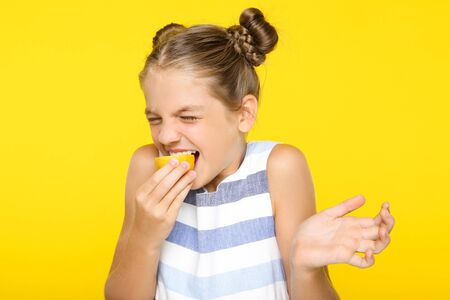 Young girl eating lemon on yellow backgroundの写真素材