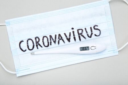Mask with text Coronavirus and thermometer on grey background