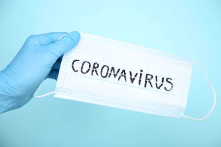 Female hand holding mask with text Coronavirus on blue backgroundの写真素材