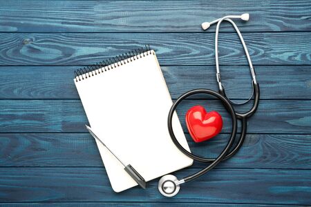 Stethoscope with notepad, red heart and pen on blue wooden tableの写真素材
