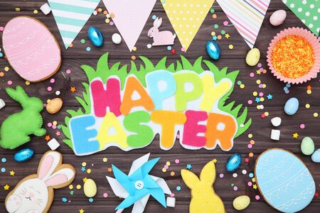 Text Happy Easter with gingerbread cookies, eggs and paper flags on wooden tableの写真素材