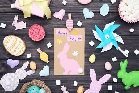 Greeting card with text Happy Easter and eggs, marshmallows, paper rabbits and windmill on wooden...