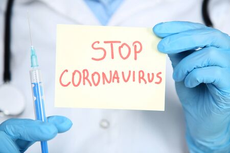 Doctor holding paper with text Stop Coronavirus and syringeの写真素材