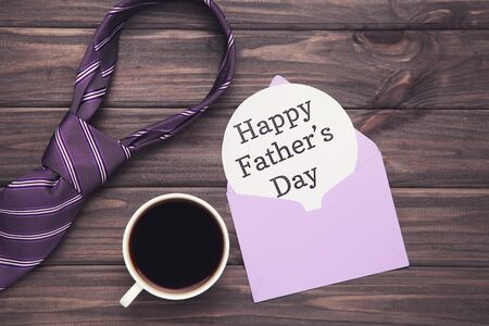 Text Happy Father's Day with cup of coffee and necktie on wooden table