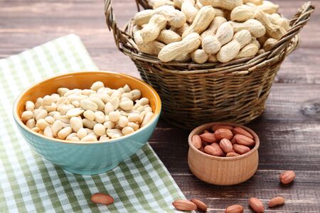 Peanuts in basket and bowl on brown wooden table