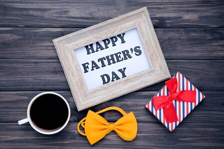 Text Happy Father's Day with cup of coffee, gift box and bow tie on wooden tableの写真素材