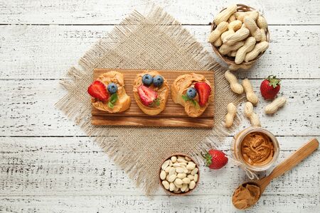 Bread with peanut butter, fruits and nuts on white wooden table
