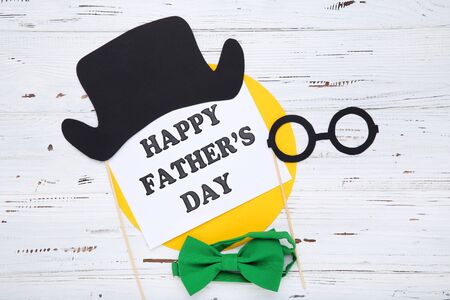 Father's day concept. Green bow tie with paper hat and eyeglasses on white wooden table