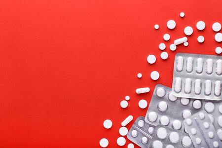 White pills in blisters on red background