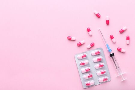 Pills with syringe on pink background