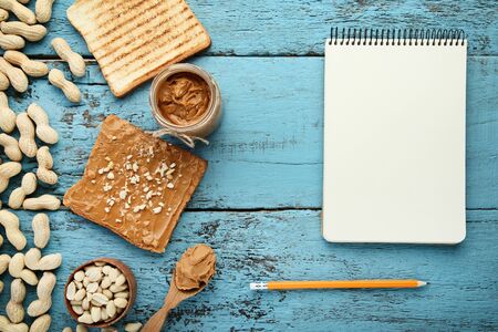 Peanut butter with bread, nuts and blank sheet of paper on wooden table