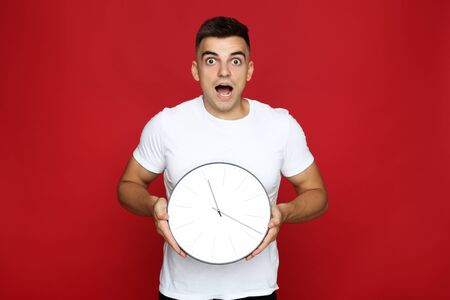 Young man with clock on red backgroundの写真素材