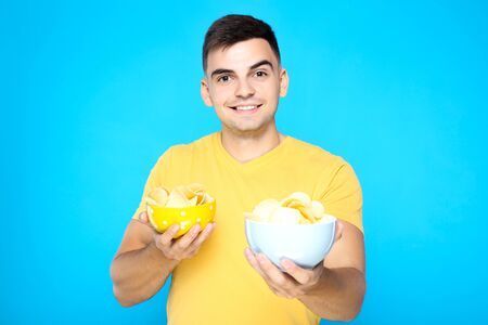 Young boy holding potato chips in bowls on blue background
