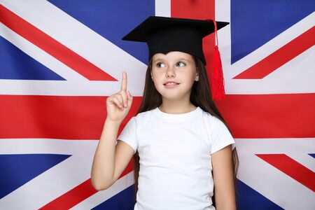 Young beautiful girl in graduation cap pointing by finger on british flag backgroundの写真素材