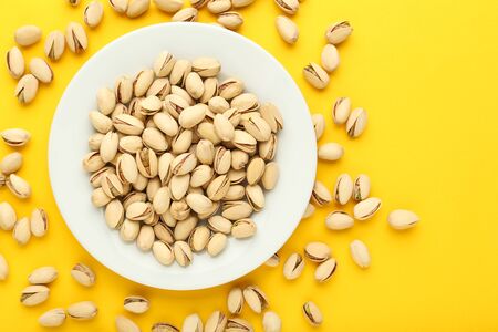 Tasty pistachios in plate on yellow backgroundの写真素材
