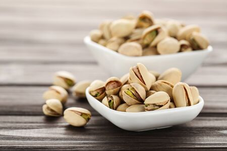 Tasty pistachios in bowls on wooden tableの写真素材