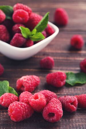 Sweet raspberries with green leafs in bowl on brown wooden tableの写真素材