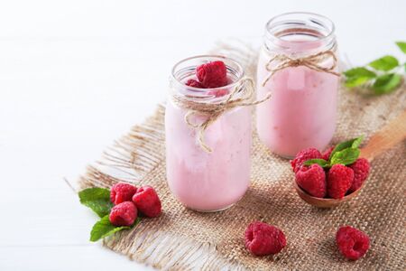 Raspberry smoothie in glass jars and spoon on white wooden tableの写真素材