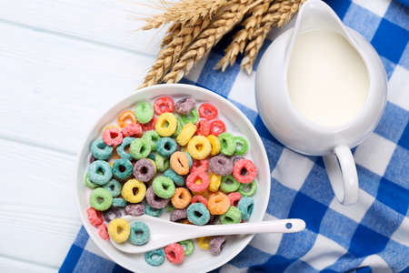 Colorful corn rings in bowl with milk and wheat ears on wooden table
