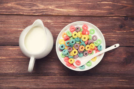 Colorful corn rings in bowl with milk and spoon on wooden table