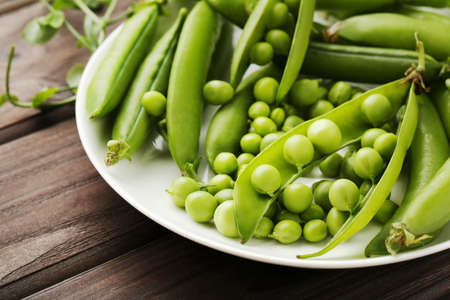 Green pea pods in plate on brown wooden tableの写真素材