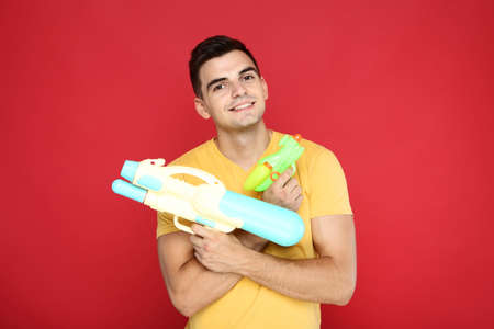 Young man with water guns on red background