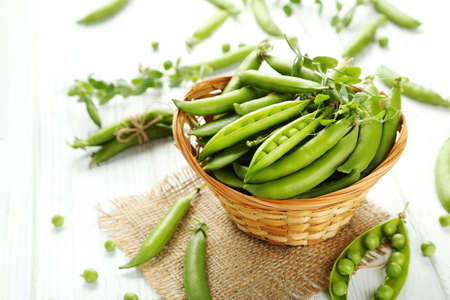 Green pea pods in basket on white wooden tableの写真素材