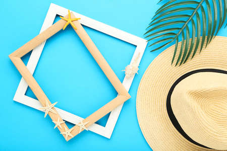Summer straw hat with palm leaf, starfishes and wooden frames on blue backgroundの写真素材