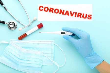 Doctor holding thermometer with medicine mask, test tube and text on paper on blue backgroundの写真素材