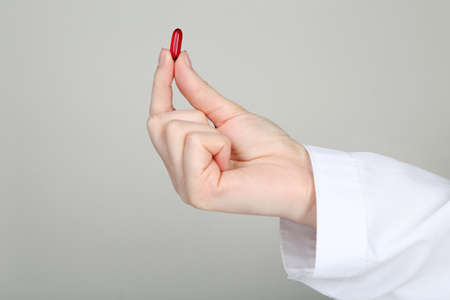 Doctor holding red capsule on gray backgroundの写真素材