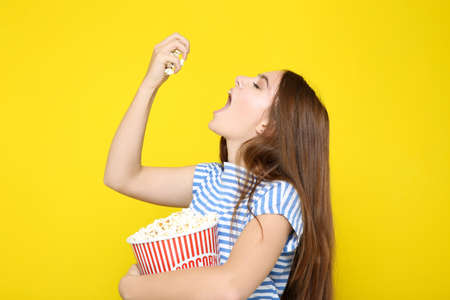 Beautiful girl eating popcorn on yellow backgroundの写真素材