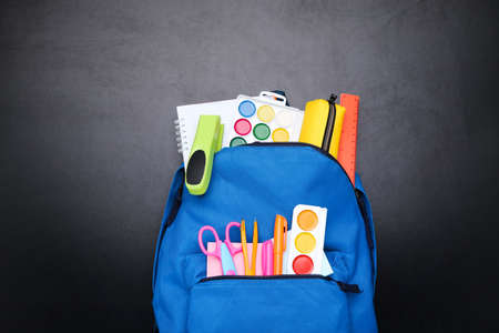Backpack with school supplies on black background