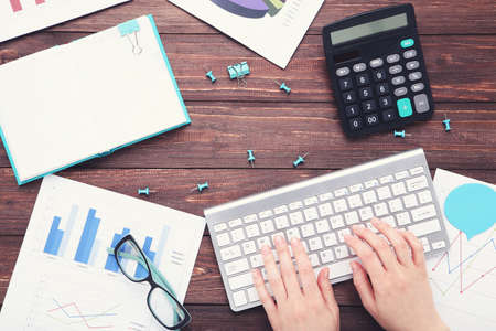 Female hands typing on computer keyboard with diagrams on paper