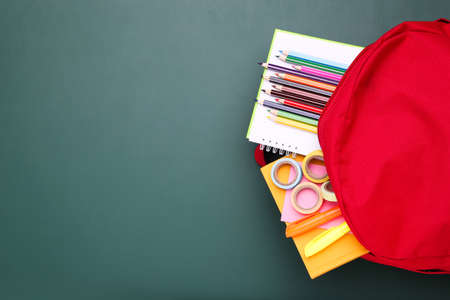 Backpack with school supplies on green background