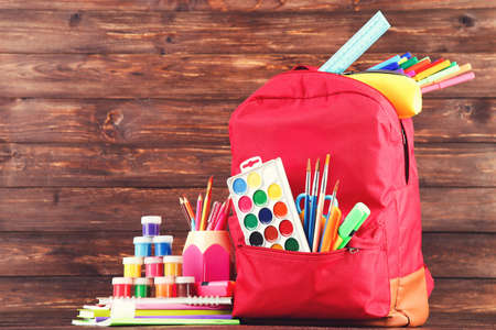 Backpack with school supplies on brown wooden background