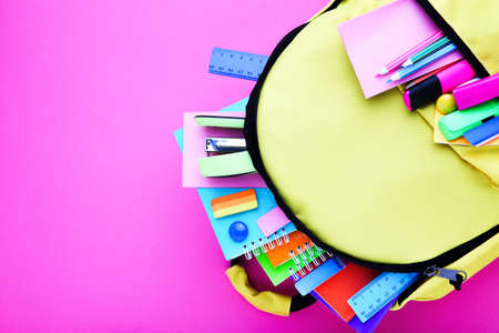 Backpack with school supplies on pink background