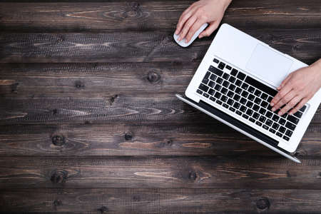 Female hands typing on laptop keyboard and using mouse on wooden tableの写真素材