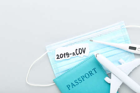 Text 2019-nCov with passport, thermometer, medicine mask and airplane model on gray background