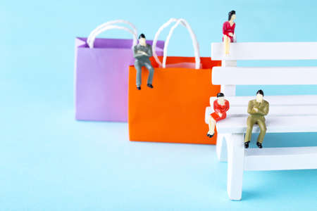 Miniature people with small wooden bench and shopping bags on blue backgroundの写真素材