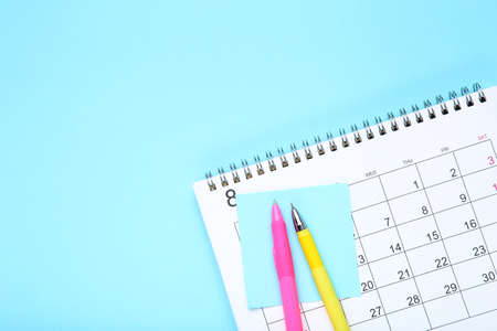 Calendar page with sticky note and pens on blue background