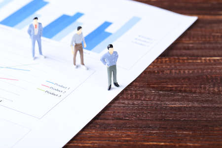 Miniature people and financial papers with graph and charts on brown wooden tableの写真素材