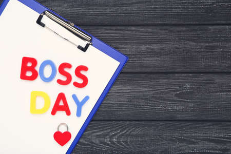 Colorful inscription Boss Day with clipboard and padlock in shape of heart on wooden black backgroundの写真素材