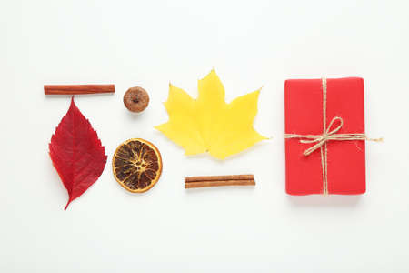Autumn leafs with gift box, cinnamon sticks, dry orange and acorn on white background