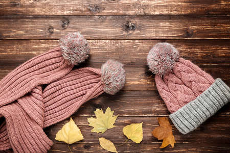 Woolen hat and scarf with autumn leafs on brown wooden tableの写真素材
