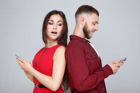 Happy young couple with mobile phones on gray backgroundの写真素材